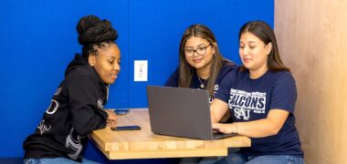 Three students in the student center looking at a laptop.